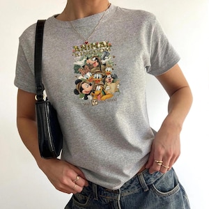 K&ouml;nnte beinhalten: Ein graues T-Shirt mit einem farbenfrohen Aufdruck von Disney-Figuren, darunter Micky Maus, Goofy und Donald Duck, mit dem Text "Animal Kingdom" und "Walt Disney World". Das Shirt hat kurze &Auml;rmel und einen Rundhalsausschnitt.