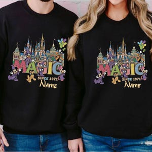 May include: Black sweatshirts with a colorful graphic featuring a castle, Mickey Mouse, and the word "MAGIC". The text "SINCE 1971" and a space for a name are also included in the design. The sweatshirts are a matching set.