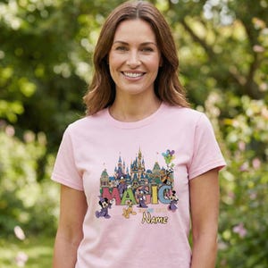 May include: A light pink t-shirt featuring a colorful graphic of a castle, cartoon characters, and the word "MAGIC". The shirt also includes the text "Name" and "Since 1971".