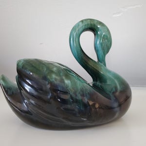 May include: A ceramic swan ornament with a glossy finish. The swan has a curved neck and a body with a gradient of dark teal to black. The ornament is a decorative item, likely for display.