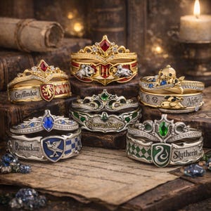 Può includere: Una collezione di anelli ornati con disegni e abbellimenti intricati. Ogni anello presenta un diverso stemma e schema di colori, tra cui oro, rosso, verde e blu. Alcuni anelli hanno testo come "Gryffindor", "Ravenclaw" e "Slytherin".