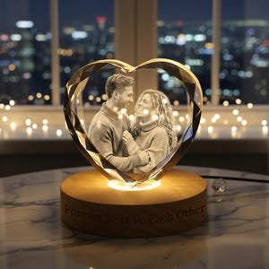 May include: A heart-shaped crystal photo frame with a picture of a couple inside. The frame sits on a wooden base that is illuminated from within. The base has the words "Forever Next To Each Other" engraved on it.