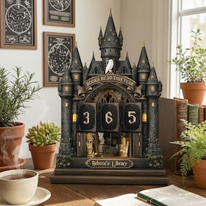 Könnte beinhalten: Ein dekorativer, burgförmiger Bücherzähler mit dem Text "BOOKS READ THIS YEAR" und den Zahlen "365". Die Burg ist dunkelgrau mit goldenen Akzenten, und eine weiße Eule sitzt auf dem zentralen Turm. Die Basis lautet "Rebecca's Library".
