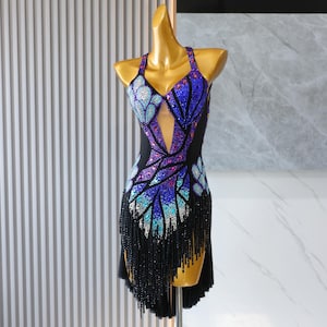 Puede incluir: Un deslumbrante vestido de baile con cuello halter, con un vibrante diseño inspirado en mariposas. El corpiño está adornado con brillantes lentejuelas azules, moradas y rosas. Flecos negros y una falda fluida completan el look elegante. Perfecto para bailes de salón o latinos.