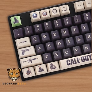 May include: Black mechanical keyboard with custom keycaps featuring images of weapons and characters. The space bar reads "CALL OF DUTY". The keyboard has a black frame and a wooden surface.