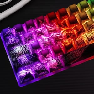 Könnte beinhalten: Nahaufnahme einer mechanischen Tastatur mit beleuchteten Tasten. Die Tasten sind mit einem Farbverlauf von Lila über Rot bis Gelb beleuchtet. Drachendesigns sind in die Oberfläche der Tastatur geätzt.