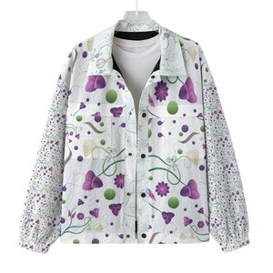 May include: White button-up jacket with a floral pattern in purple, green, and beige. The jacket has a textured surface and long sleeves with a patterned design. The jacket is hanging on a white hanger.
