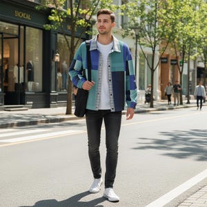 Könnte beinhalten: Eine Person trägt eine Patchwork-Jacke in Blau- und Türkistönen, ein weißes T-Shirt und eine schwarze Jeans. Die Jacke hat einen Kragen und eine Knopfleiste. Weiße Turnschuhe und eine schwarze Umhängetasche vervollständigen den Look. Die Person geht auf einer Straße.