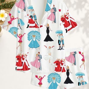 May include: A white short-sleeve button-down pajama shirt and matching shorts set featuring a repeating print of vintage-style dancers in various outfits, including red Santa-inspired costumes, pink dresses, black gowns, and blue feathered fans.