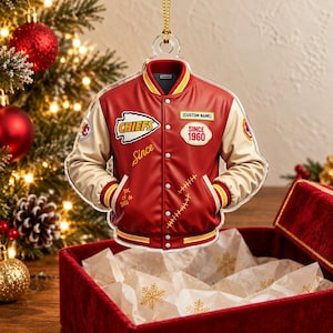 May include: A red and cream varsity jacket ornament featuring a white arrowhead logo with the text CHIEFS, a patch reading SINCE 1960, and a custom name label. The jacket has a button-front closure, ribbed cuffs, and gold-colored hanging cord.