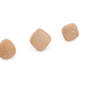 May include: Three small, light brown wooden beads in various geometric shapes: a rounded triangle and two square-like shapes with rounded corners. The beads are arranged on a white background, showcasing their natural wood grain texture.