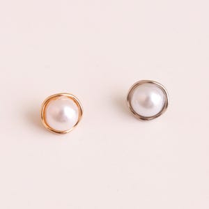 May include: Two stud earrings featuring round white pearls set in irregular, organic-shaped metal frames. One earring has a warm gold-toned metal setting, while the other earring features a cool silver-toned metal setting, both with a smooth finish.