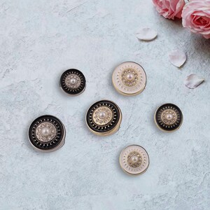 Puede incluir: Una variedad de espejos compactos decorativos en varios tamaños y diseños. Los espejos presentan adornos de perlas y pedrería, con esquemas de color negro, dorado y blanco. Rosas rosas y pétalos en el fondo.