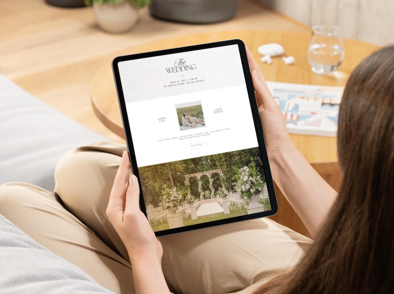 May include: A tablet displaying a digital wedding invitation website. The screen shows the text THE WEDDING, a date, a location, a small square photograph of a couple, and a large image of an outdoor wedding ceremony venue with stone arches.