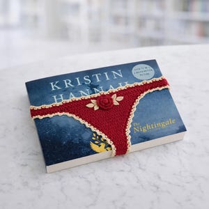 May include: A white ceramic mug with a black handle and the text "But First, Coffee" in a bold, black font. The mug is set against a blurred background, suggesting a cozy setting.