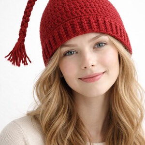 A red knitted hat with a long, plaited tail and a tassel. The hat is a deep shade of red and has a textured appearance. A winter accessory.