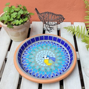 May include: A blue and green mosaic bird bath featuring a bluebird design. The bird bath is made of ceramic and has a round shape.