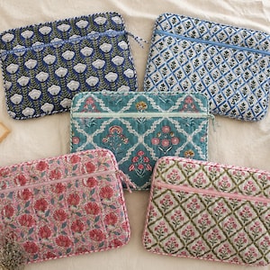 May include: Five rectangular quilted laptop sleeves featuring various floral and geometric block print patterns in shades of blue, teal, pink, and green. Each sleeve includes a horizontal zippered pocket on the front and matching fabric trim.