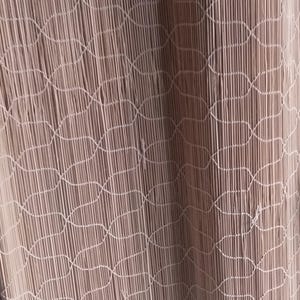 May include: A light beige string curtain featuring a vertical arrangement of thin, hanging threads. The curtain is accented with a repeating, woven net-like pattern that connects the individual strands across the entire length of the fabric.