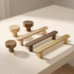 May include: A collection of cabinet hardware including three round knobs and three rectangular pulls. Each piece features a hammered, textured surface and is finished in varying shades of metallic gold and bronze tones for a cohesive look.