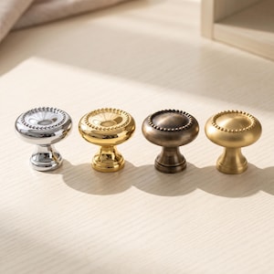 May include: Four round cabinet knobs arranged in a row, each featuring a beaded edge detail. The knobs are finished in four distinct metallic tones: polished chrome, bright gold, antique bronze, and a soft matte brushed gold finish.