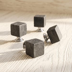 May include: A set of four cabinet knobs, each featuring a dark grey, textured stone cube head mounted on a polished silver-tone metal base. The square stone elements have a matte, natural finish, while the circular metal bases provide a reflective contrast.
