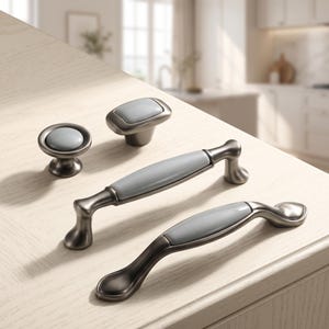 May include: A collection of four cabinet hardware pieces featuring a dark metallic finish and smooth, light gray ceramic inserts. The set includes two round and rectangular knobs alongside two arched drawer pulls with matching gray center accents.