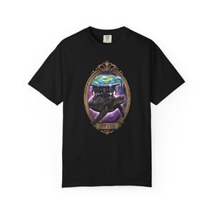 May include: Black t-shirt featuring a detailed illustration of a turtle carrying a flat Earth on its back, framed within an ornate gold oval. The design includes the text "GREAT A'TUIN" at the bottom, with a colorful galaxy background.