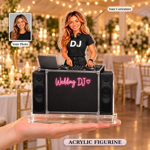 Op de afbeelding: Een op maat gemaakt acrylfiguur met een karikatuur van een persoon met lang bruin haar in een zwart t-shirt met de tekst DJ, staand achter een zwarte DJ-booth met twee luidsprekers en de neonroze tekst Wedding DJ met een hartje.