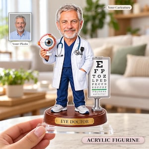 Könnte beinhalten: Eine Acrylfigur eines Augenarztes mit grauem Haar, der einen weißen Kittel über blauer Arbeitskleidung und ein Stethoskop trägt. Die Figur hält ein Augenmodell und steht neben einer Sehtafel auf einem Holzsockel mit der Aufschrift EYE DOCTOR.