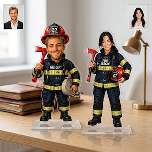 Könnte beinhalten: Zwei personalisierte Acryl-Aufsteller, die einen Feuerwehrmann und eine Feuerwehrfrau in dunkelblauen Uniformen mit gelben Reflexstreifen zeigen. Beide Figuren halten eine rote Axt und tragen einen Helm mit der Aufschrift 27. Der Feuerwehrmann hält einen aufgerollten Schlauch, die Feuerwehrfrau einen roten Helm. Beide stehen auf transparenten rechteckigen Sockeln.