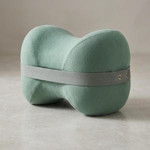 以下が含まれることがあります： グレーのストラップが付いた、明るい緑色の膝枕。 枕は湾曲した形状で、脚をサポートするように設計されています。 ストラップは2つの金属リベットで固定されています。 枕は柔らかく、質感のある素材で作られています。