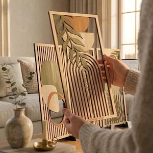 Peut inclure: Décoration murale en bois avec des formes géométriques superposées, des arches et des motifs de feuilles dans des tons de marron, vert et orange. L'œuvre a une finition en grain de bois naturel et le texte "STUDIO AETENA".