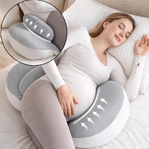 May include: A grey and white pregnancy pillow for side sleeping. The pillow has a curved design to support the back and belly, with a smaller head pillow. The image shows a person sleeping on the pillow.