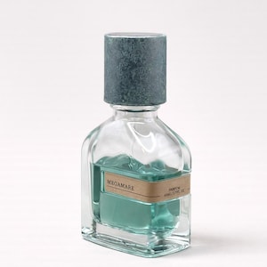 Könnte beinhalten: Eine transparente Parfümflasche aus Glas mit türkisfarbener Flüssigkeit und einem strukturierten, grauen Verschluss. Die Flasche hat eine rechteckige Form mit abgerundeten Kanten. Das Etikett lautet "MEGAMARE".