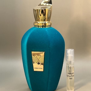 Puede incluir: Un frasco de perfume turquesa con tapón dorado y un pequeño vial de muestra. El frasco tiene un aspecto texturizado, aterciopelado, y una etiqueta dorada que dice "ERBA PURA". El vial de muestra está etiquetado "Xerjoff Erba Pura 5ml".