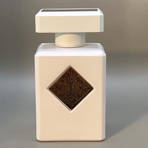 Peut inclure: Flacon de parfum rectangulaire blanc avec un dessus carr&eacute; et un embl&egrave;me d&eacute;coratif de couleur bronze. Le flacon a un bouchon blanc et un dessus rectangulaire bronze.