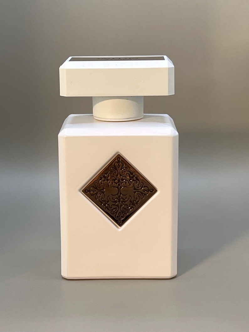 Peut inclure: Flacon de parfum rectangulaire blanc avec un dessus carr&eacute; et un embl&egrave;me d&eacute;coratif de couleur bronze. Le flacon a un bouchon blanc et un dessus rectangulaire bronze.