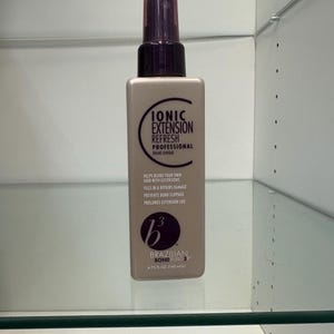 May include: A rectangular bottle of Ionic Extension Refresh Professional hair product. The bottle is beige with a dark purple spray top. Text on the label includes "HELPS BLEND YOUR OWN HAIR WITH EXTENSIONS" and "4.75 fl oz (140 ml)."