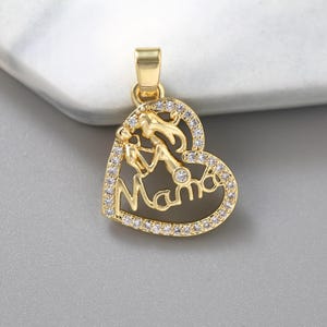 May include: A gold-colored pendant in the shape of a heart, featuring the word "Mama" in cursive script. The pendant has a mother and child silhouette and is encrusted with small, clear gemstones. The bail is a simple rectangular shape.