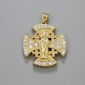May include: A gold-colored pendant in the shape of a cross, adorned with clear gemstones and a central figure. The cross design features intricate detailing and a bail for a chain. The pendant is set against a gray background.