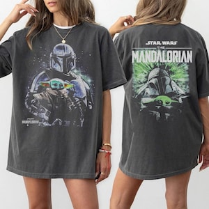 Puede incluir: Camiseta gris oscuro con un gr&aacute;fico de The Mandalorian y Grogu de Star Wars. La parte delantera de la camiseta muestra a los personajes en una escena espacial, mientras que la parte trasera muestra el logotipo del programa y los personajes en verde.