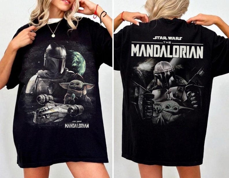 May include: Black t-shirt featuring a graphic of The Mandalorian and Grogu from Star Wars. The front design shows the characters and a spaceship against a space background. The back of the shirt displays the Star Wars logo and "The Mandalorian".
