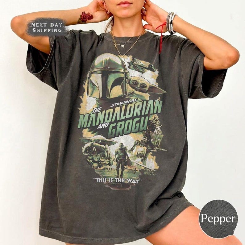 May include: Pepper-colored t-shirt featuring a graphic from the Star Wars series, "The Mandalorian and Grogu." The design includes images of the Mandalorian, Grogu, and the text "This is the Way."