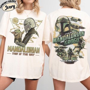 May include: Ivory-colored t-shirts featuring "The Mandalorian and Grogu" graphics. The front design shows the Mandalorian and Grogu, with the text "MANDALORIAN - THIS IS THE WAY." The back design includes the Star Wars logo and additional characters.