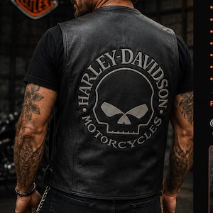 May include: A black leather vest featuring a large embroidered Harley-Davidson skull logo on the back. The vest is sleeveless with visible stitching and is worn over a black t-shirt. Text on the image includes Harley-Davidson Genuine Leather Vest.