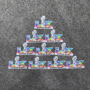 May include: A collection of Super Bowl patches arranged in a pyramid shape. Each patch features the Super Bowl trophy and the text "SUPER BOWL" in a colorful design with blue, yellow, and pink accents. The patches are on a gray background.