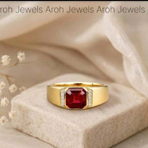 Könnte beinhalten: Ein goldener Ring mit einem quadratisch geschliffenen roten Edelstein in der Mitte, der von zwei vertikalen Reihen kleiner weißer Steine flankiert wird. Die Ringschiene ist glatt und poliert. Der Text Aroh Jewels steht oben im Bild.