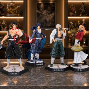 Könnte beinhalten: Vier detaillierte Figuren von Anime-Charakteren. Die Figuren befinden sich in dynamischen Posen mit leuchtenden Farben und komplizierten Details. Jede Figur steht auf einer sechseckigen Basis mit japanischem Text. Der Hintergrund zeigt zusätzliche Figuren und dekorative Beleuchtung.