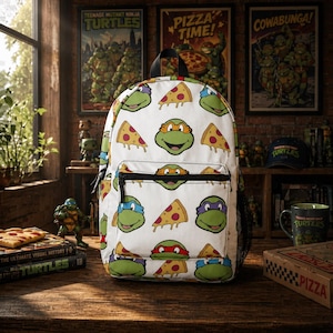 May include: White backpack featuring Teenage Mutant Ninja Turtles faces and pizza slices. The backpack has a black top handle, a front pocket, and a side mesh pocket. The background includes framed posters, a mug, and a pizza box.